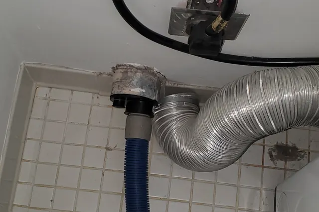 Foil dryer vent transition behind a clothes dryer, with the Fresh vacuum hose connected