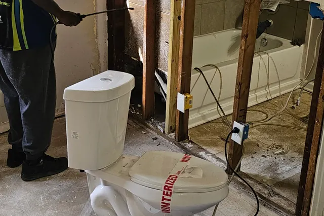Bathroom walls opened for drying after water damage, with an air mover running